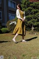 A woman in a yellow dress is walking in the grass.