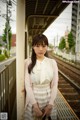 A woman standing on a train platform holding a handbag.