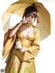 A woman in a yellow kimono holding an umbrella.