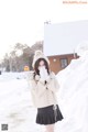 A woman standing in the snow wearing a hat and gloves.