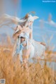 A woman in a white dress standing in a field of tall grass.