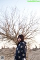 A woman standing in front of a bare tree in the desert.