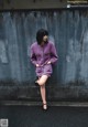 A woman in a purple dress leaning against a wall.